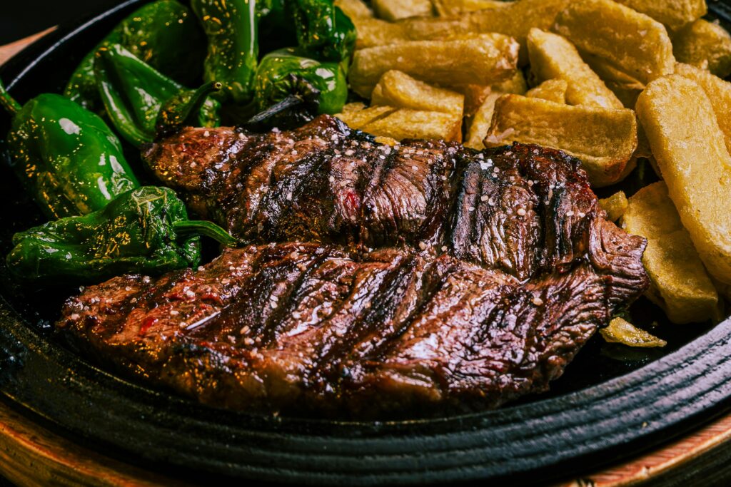 Juicy grilled beef steak with green peppers and crispy potatoes on a plate.