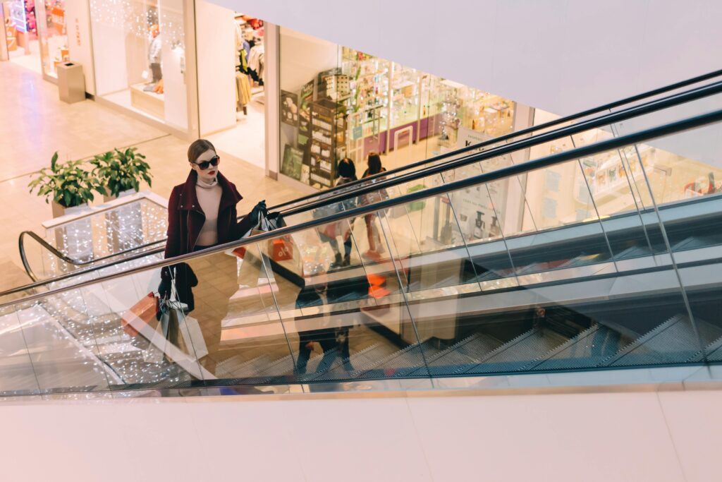 A fashionable woman ascends an escalator in a chic, modern shopping mall.