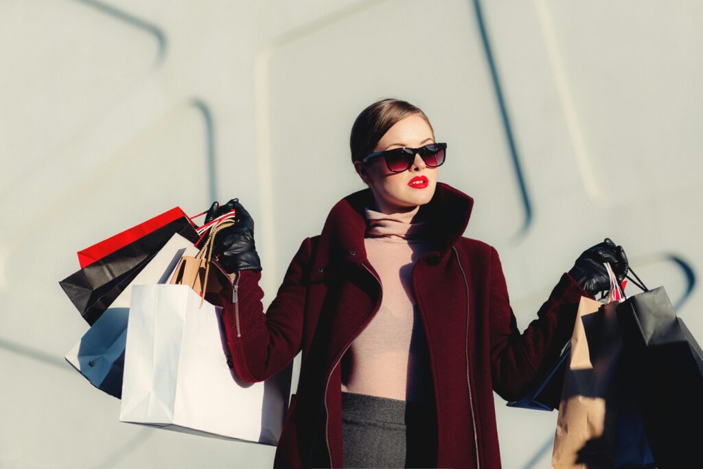 Stylish young woman in sunglasses carrying shopping bags outdoors. Elegant fashion statement.