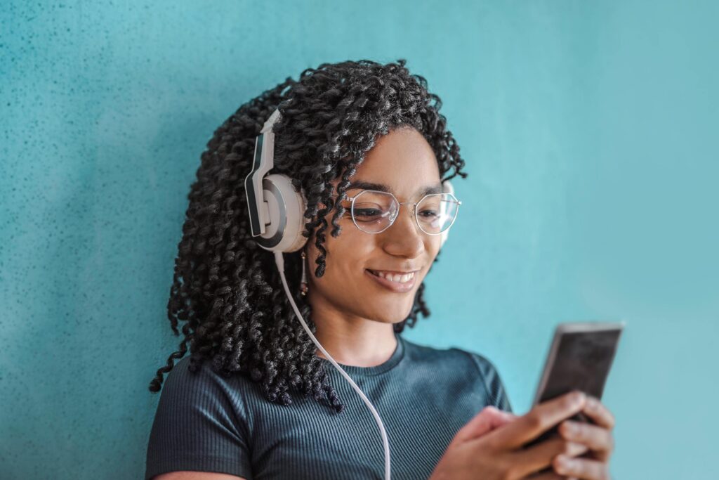 Portrait of a happy woman using headphones and smartphone against a blue wall.