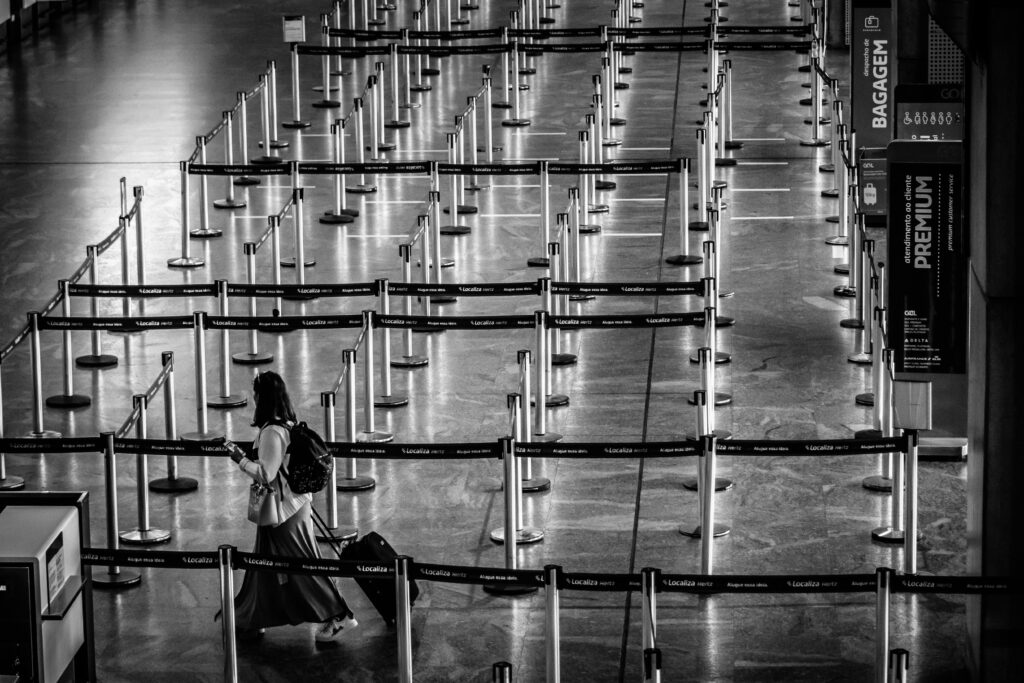From above black and white side view of unrecognizable female tourist with backpack and suitcase strolling on fenced passage in airport