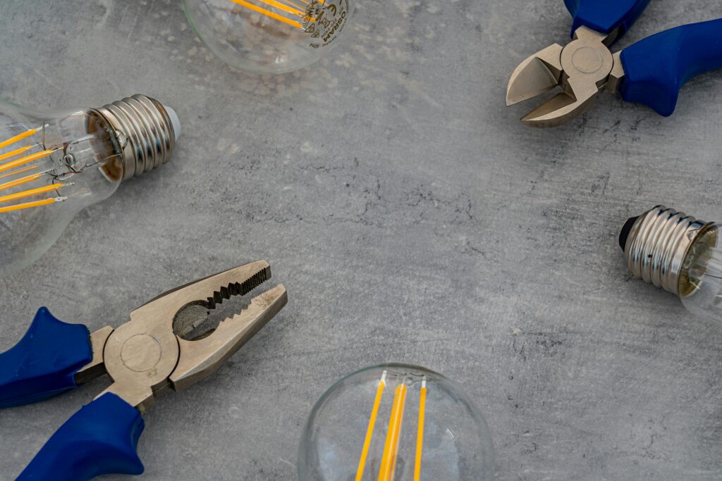 Top view of Edison bulbs and blue-handled pliers arranged on a gray concrete surface.