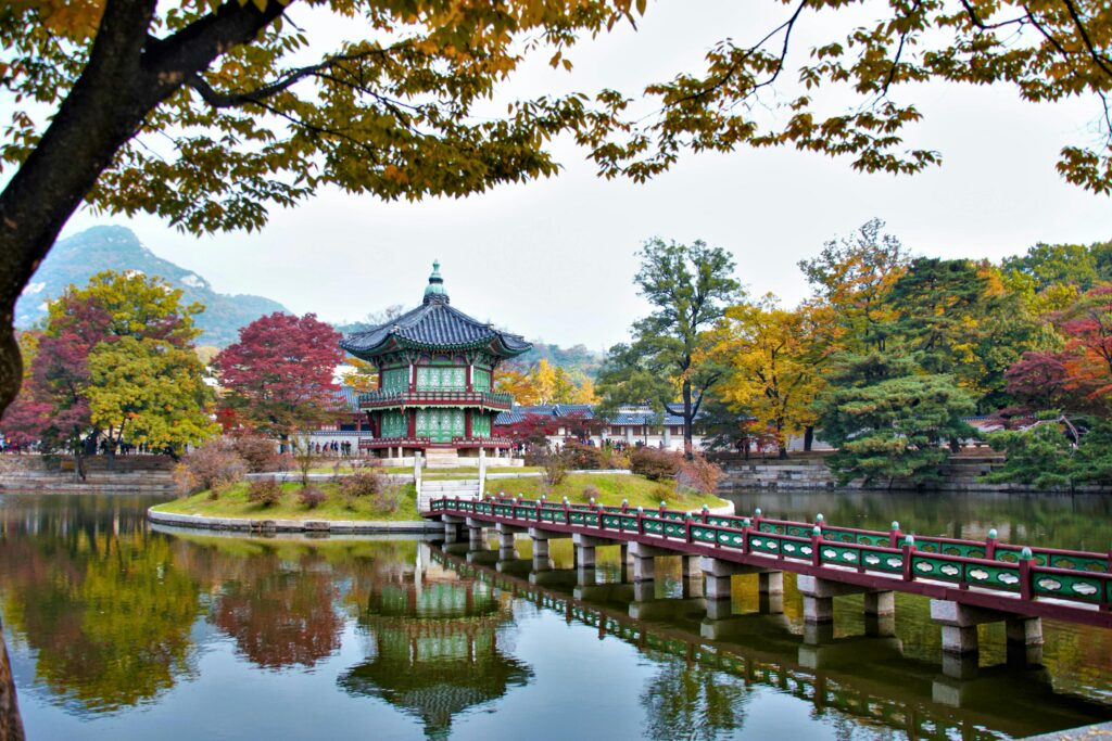 Tranquil autumn scene at Gyeongbokgung Palace with colorful trees and a serene lake reflection.