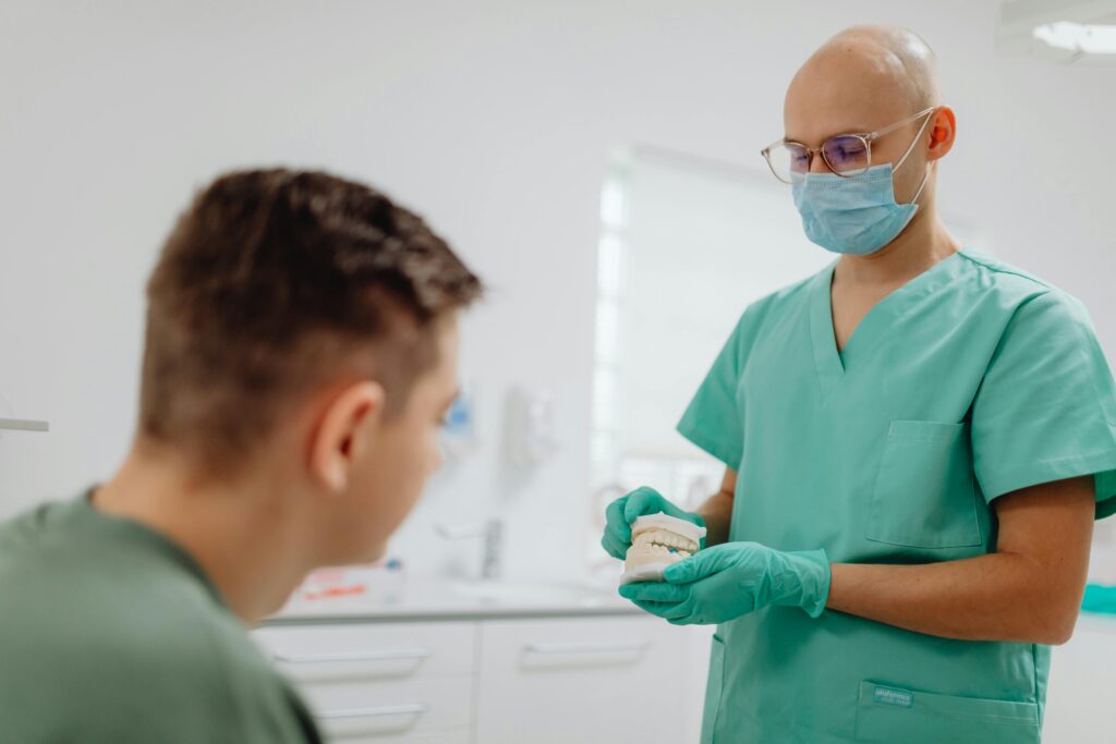 Dentist in scrubs explains dental procedure to a patient in an office setting.