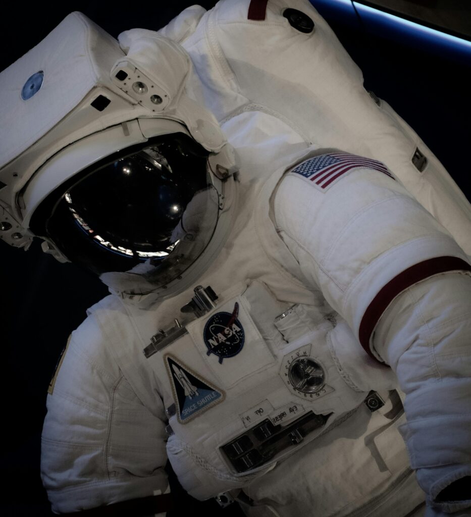 Close-up of an astronaut in a NASA space suit with the US flag, outdoors at Kennedy Space Center.