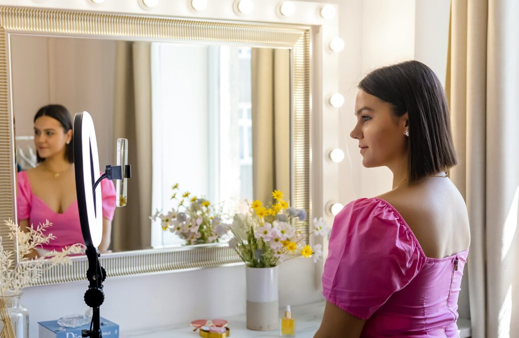 A young woman records a vlog using a ring light in front of a stylish mirror.
