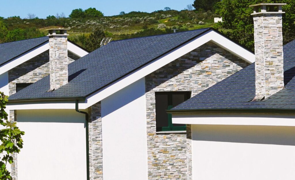Row of modern suburban houses with chimneys in a sunny rural setting, surrounded by greenery.